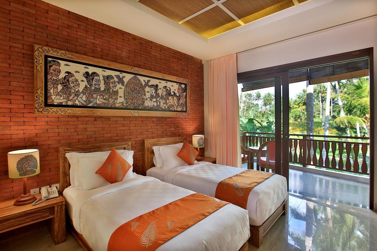 A hotel room with two beds, a large mural on the wall, a balcony with a view of palm trees.