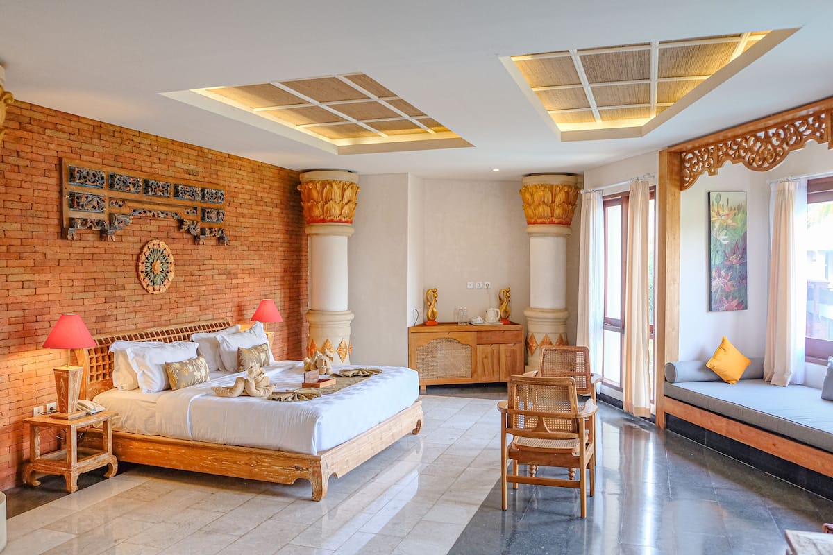 A spacious bedroom with a large bed, a wooden nightstand, a wooden dresser, and a seating area with a sofa and chairs.