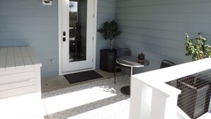 A small patio with a white door, a round table, a potted plant, and a black chair. - Modern Studio Apartment., Sleeps 4, Steps to the Beach! (Santa Rosa Beach)