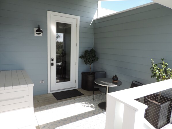 A small patio with a white door, a round table, a potted plant, and a black chair.