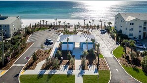 A parking lot with a building in the center, surrounded by palm trees and a beach view. - Modern Studio Apartment., Sleeps 4, Steps to the Beach! (Santa Rosa Beach)