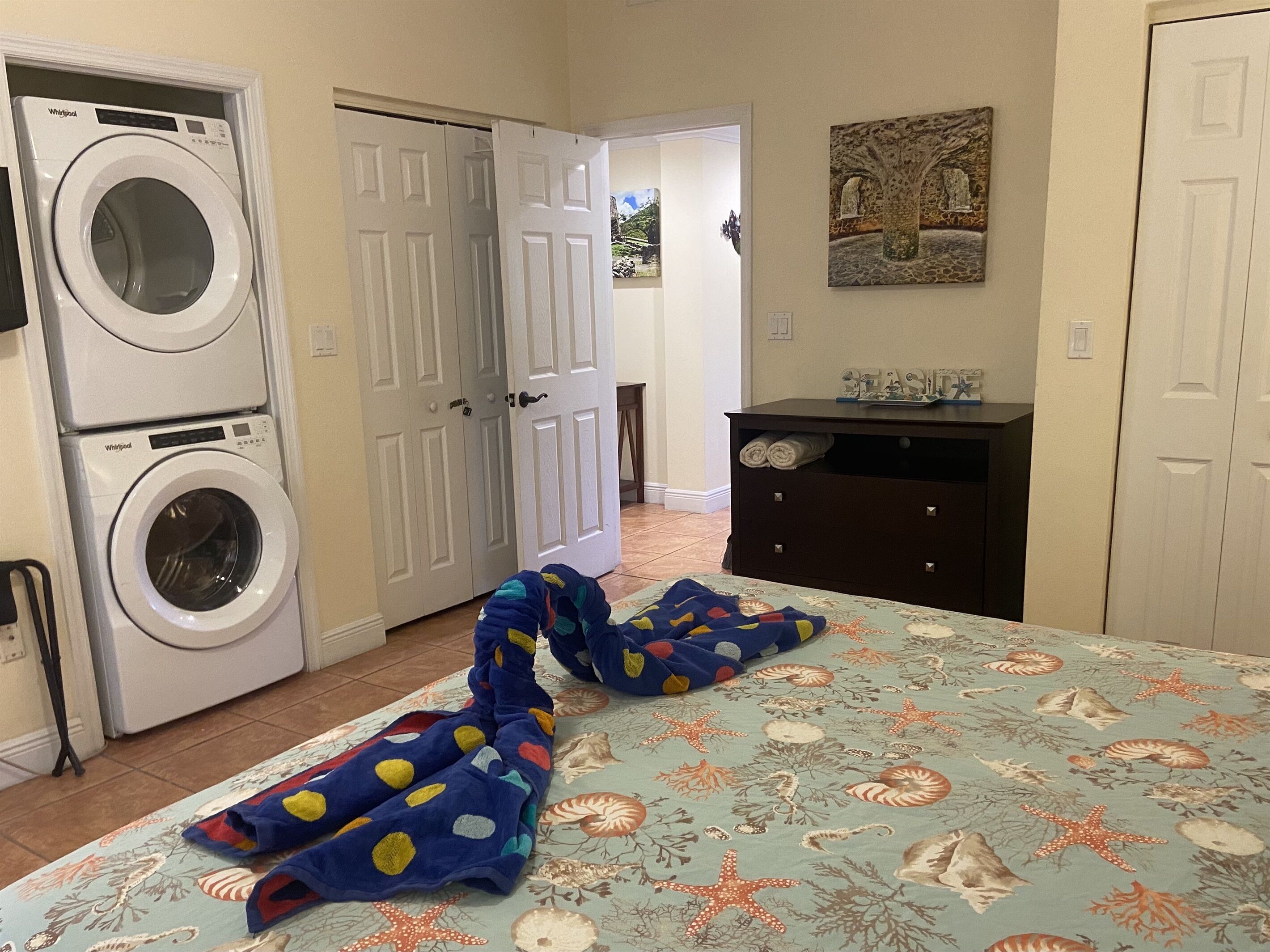 Une chambre à coucher comprenant un lit, une machine à laver, une commode et une porte donnant sur une autre pièce.