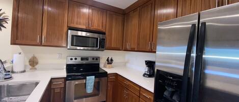 A modern kitchen with wooden cabinets, stainless steel appliances including a microwave, oven, and refrigerator, and a white countertop.