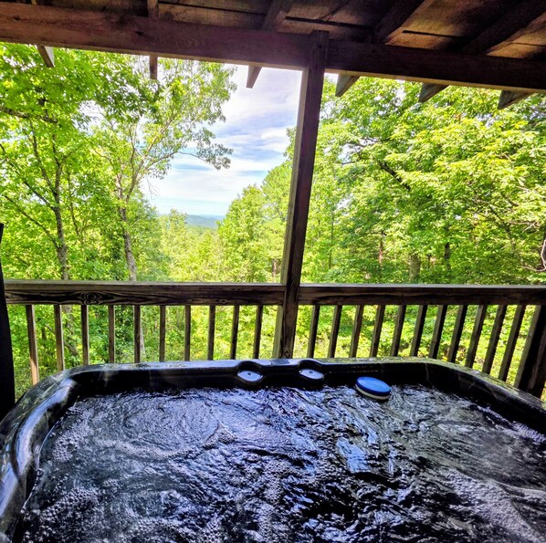A hot tub with a wooden deck and a view of a forested landscape.