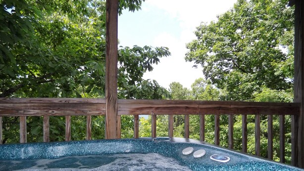 A hot tub with a wooden deck and a view of lush green trees. - Nite Vu Cabin:A Light and Airy Retreat with Mountain Views, Hot Tub, and Jacuzzi (Sevierville)