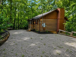 A wooden cabin with a porch and a chimney, surrounded by trees.