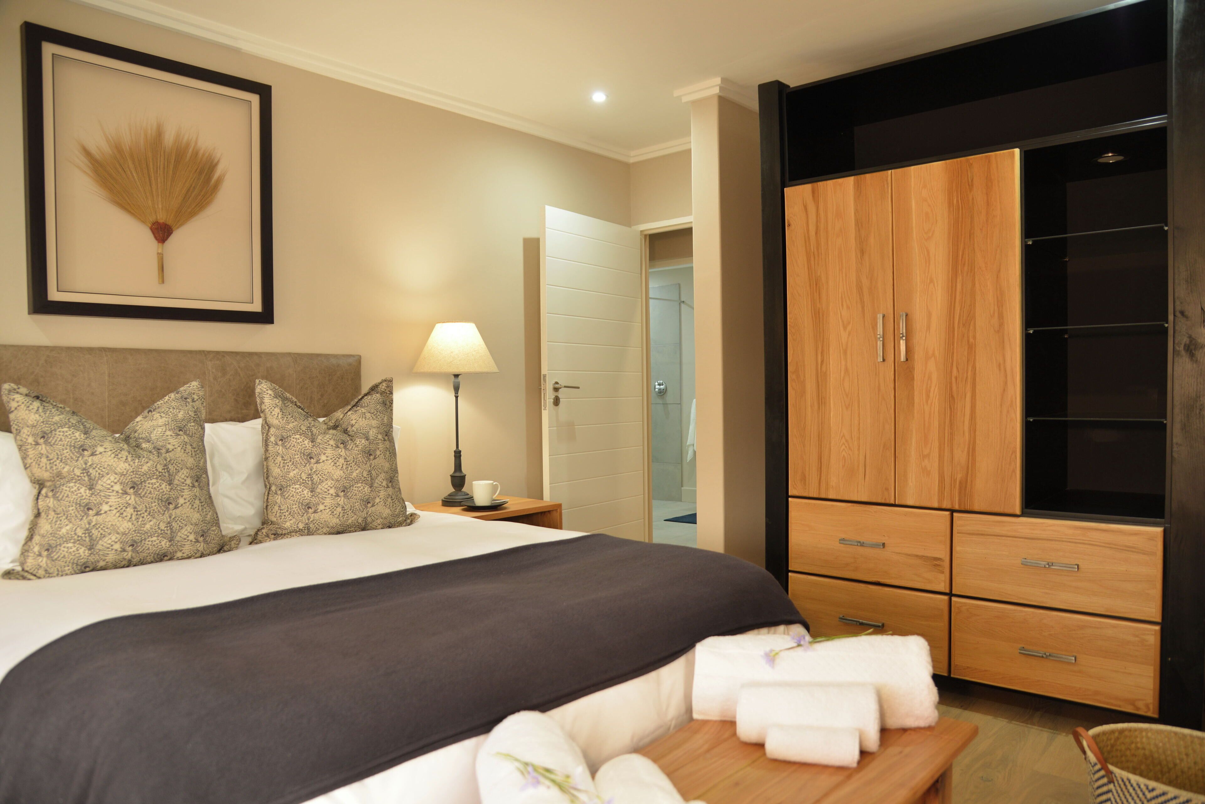 A hotel room with a bed, a bedside table with a lamp, a wardrobe, and a framed picture on the wall.