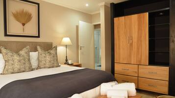 A hotel room with a bed, a bedside table with a lamp, a wardrobe, and a framed picture on the wall.