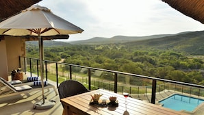 Een balkon met een houten tafel, stoelen, een tafel met glazen blad, een zwembad en uitzicht op het landschap.