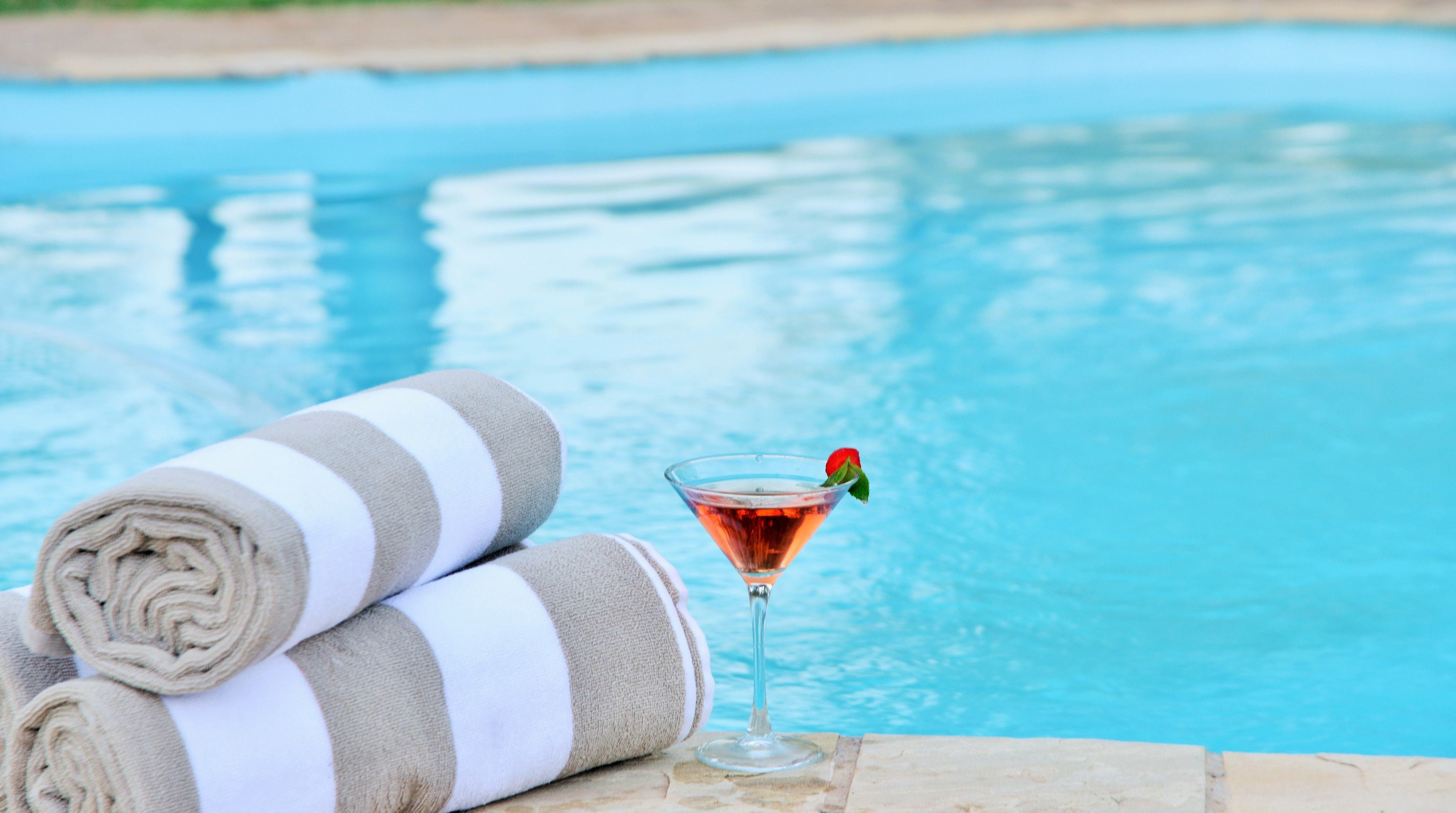 A poolside setting with a rolled towel and a martini glass with a garnish.