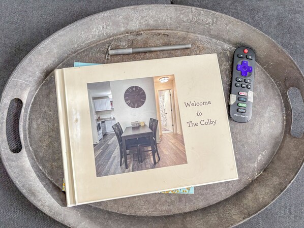 A welcome mat with a remote control and a book on a tray.