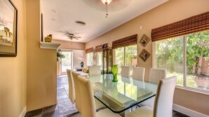Un comedor con mesa de vidrio, sillas blancas y ventilador de techo.