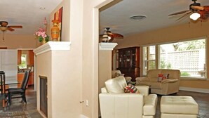 Un salón espacioso con chimenea, ventilador de techo y un ventanal con persianas.