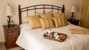 A neatly made bed with a tray of breakfast items, a wooden nightstand with a lamp, and a wooden cabinet.