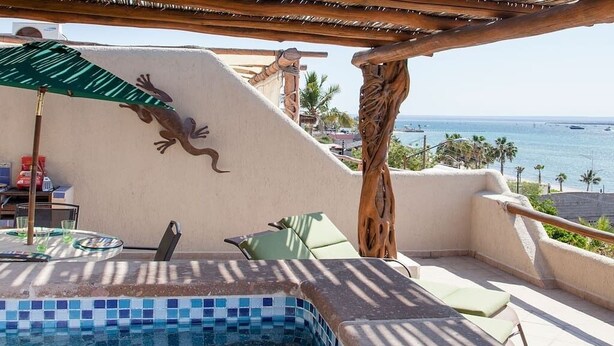 A rooftop pool area with a view of the ocean, a wooden pergola, and lounge chairs.