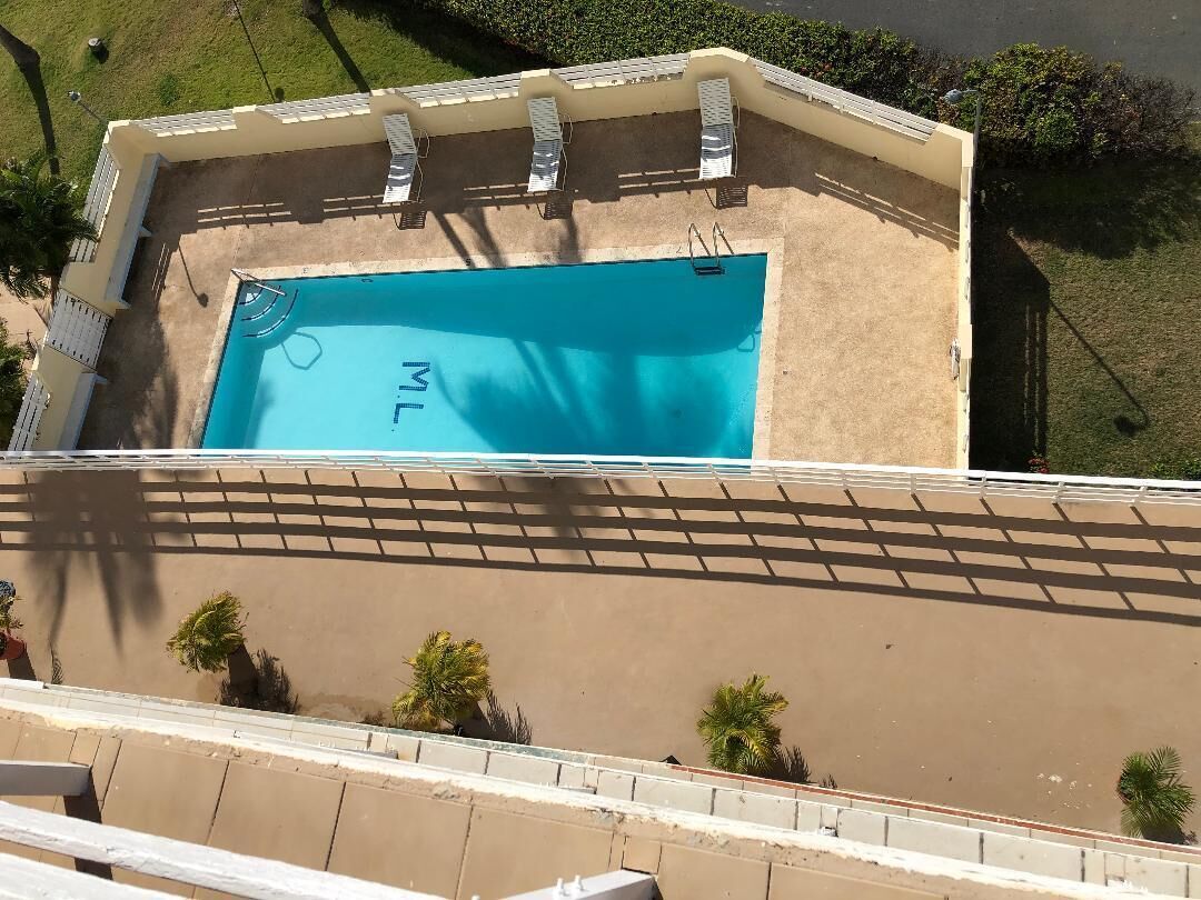 An aerial view of a swimming pool with a 'L' logo, surrounded by a beige deck and white railings.