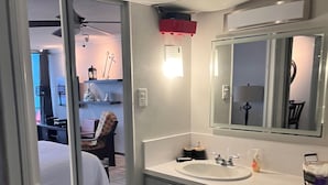 Ein Badezimmer in einem Hotel mit einem großen Spiegel, einem Waschbecken und einer Toilette. Vor der Toilette liegt ein kleiner Teppich.