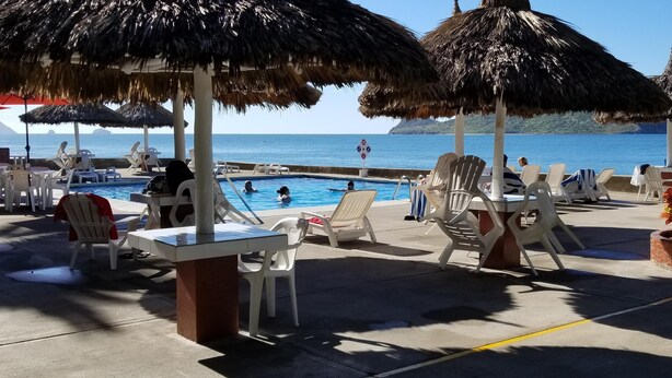 A poolside area with thatched umbrellas, lounge chairs, and a view of the sea.