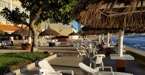 A beachside seating area with thatched umbrellas and white plastic chairs.