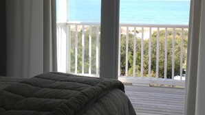 A bedroom with a view of the ocean through a balcony railing.