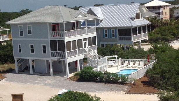A two-story beachfront house with a balcony, a swimming pool, and a covered deck area.
