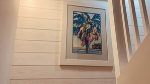 A staircase with a framed artwork of a palm tree, wooden paneling on the walls, and a window above.