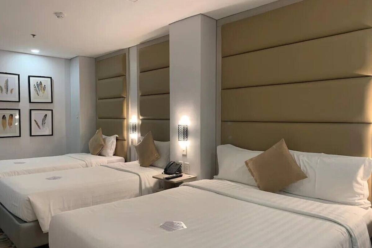 A hotel room with two beds, beige headboards, and framed artwork on the wall.