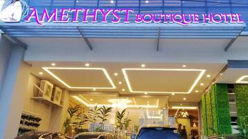 The Amethyst Boutique Hotel entrance with a modern design, featuring a neon sign, a glass facade, and several parked cars.
