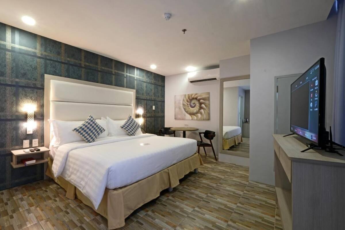 A modern hotel room with a large bed, bedside tables, a flat-screen TV, and a small desk area.