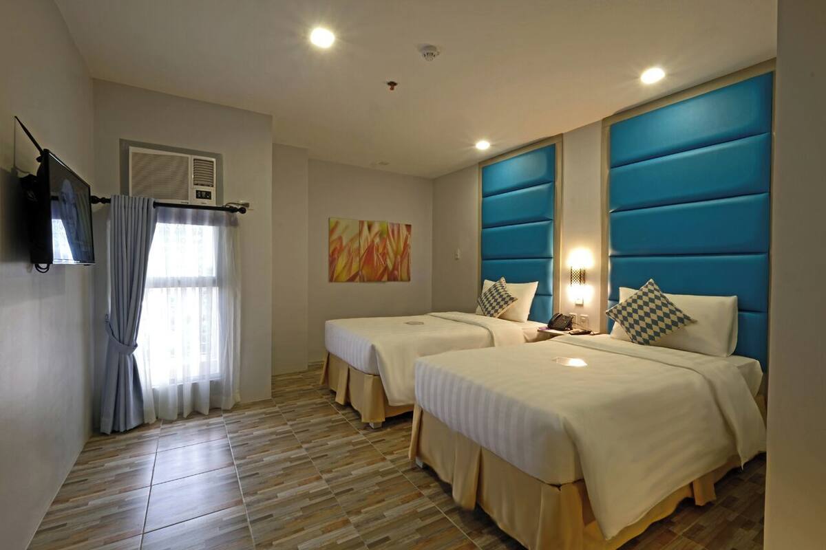A hotel room with two beds, a TV, and a painting on the wall.