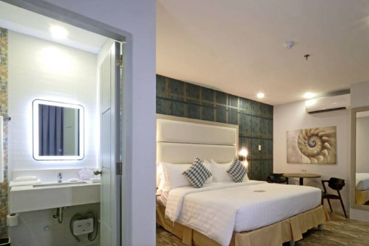 A hotel room with a bed, bedside table, mirror, and a painting on the wall.