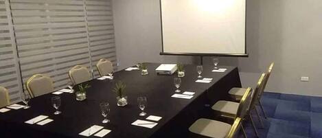 A conference room with a long table, chairs, a projector screen, and small potted plants.