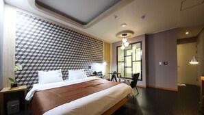 A modern hotel room with a large bed, a geometric patterned wall, a small table with chairs, and a large window. - Legend Motel (Geoje)