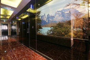 Un hall d’hôtel moderne avec un sol en marbre, des ascenseurs en verre et une grande fenêtre donnant sur un paysage montagneux.