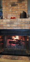 A fireplace with a stone wall, a fire burning inside, and a metal screen.