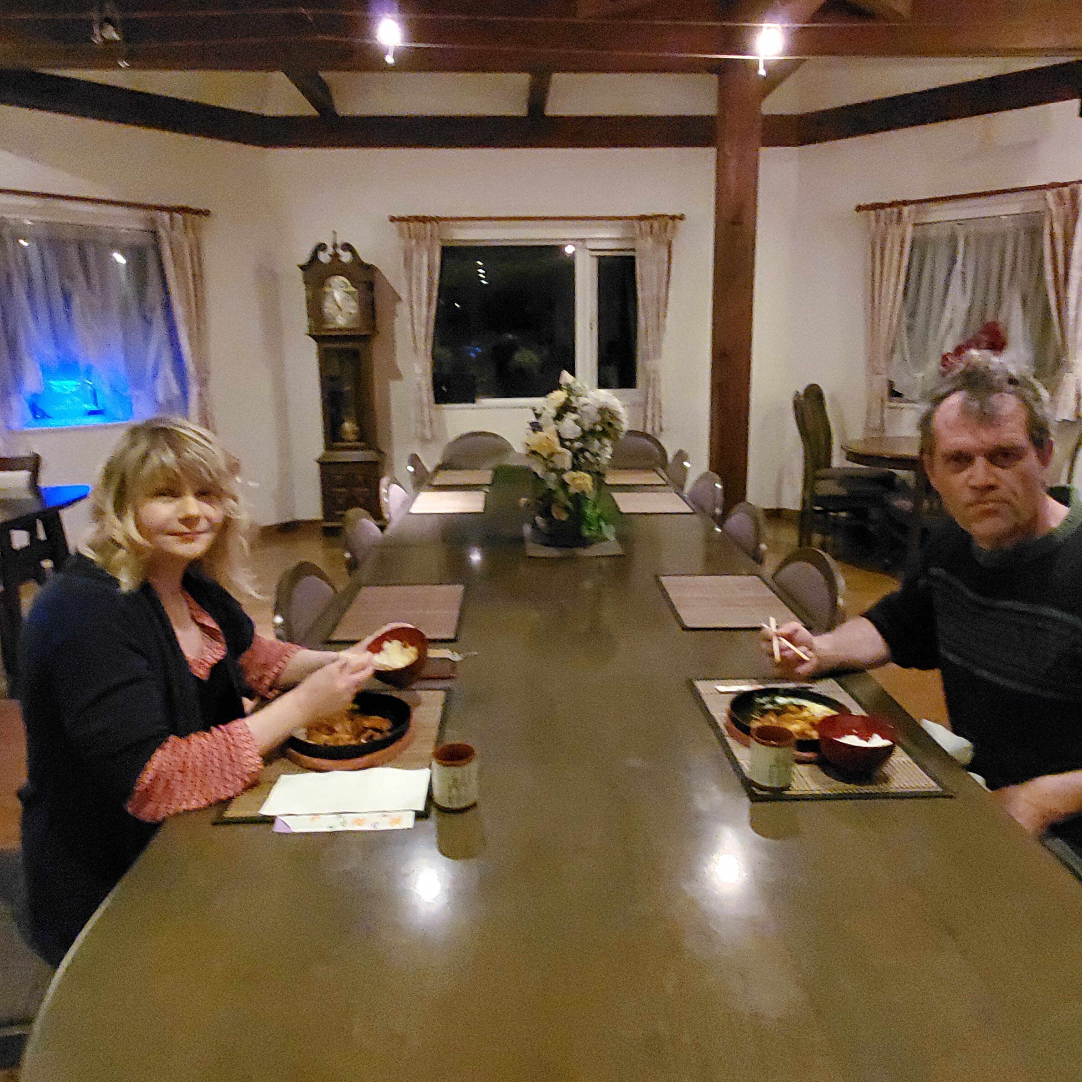 Un espace repas avec une longue table, des chaises et un vase de fleurs placé au centre.
