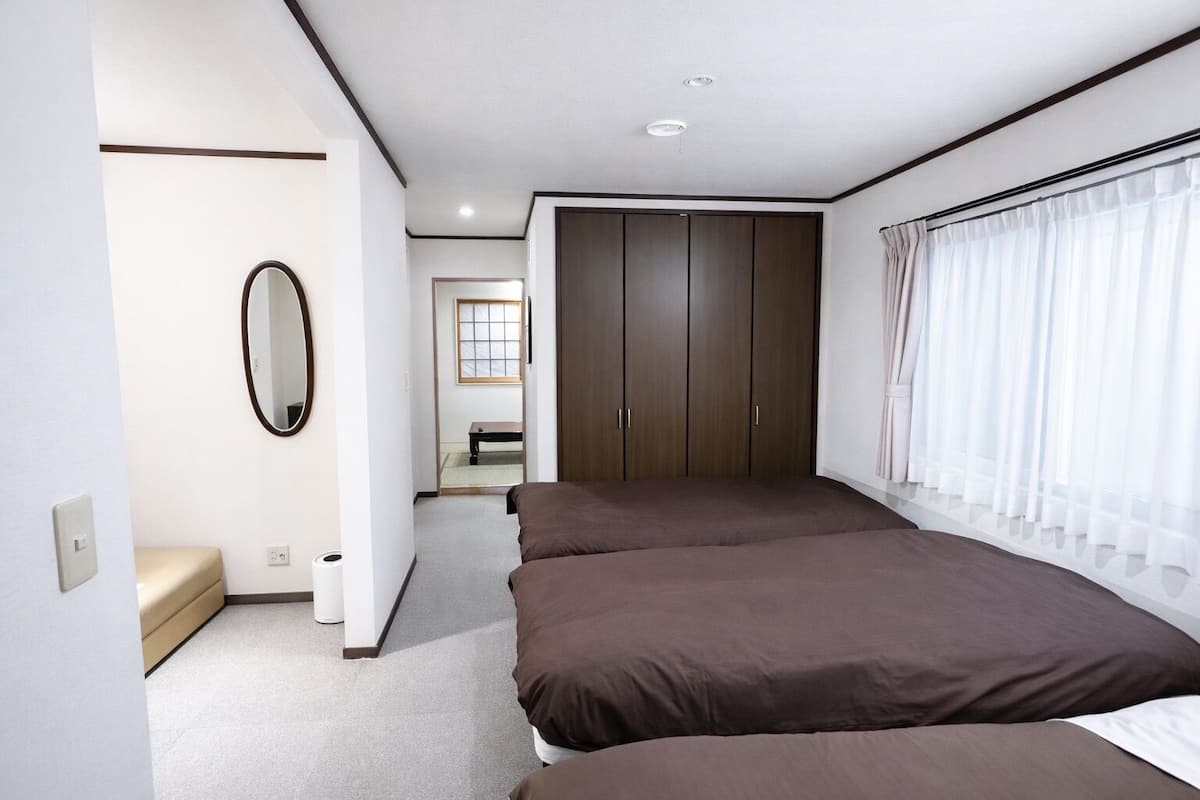 A bedroom with a bed, a wardrobe, a mirror, and a window with curtains.