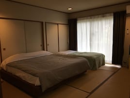 Habitación de hotel con dos camas, un ventanal grande con cortinas y un equipo de aire acondicionado a la vista.