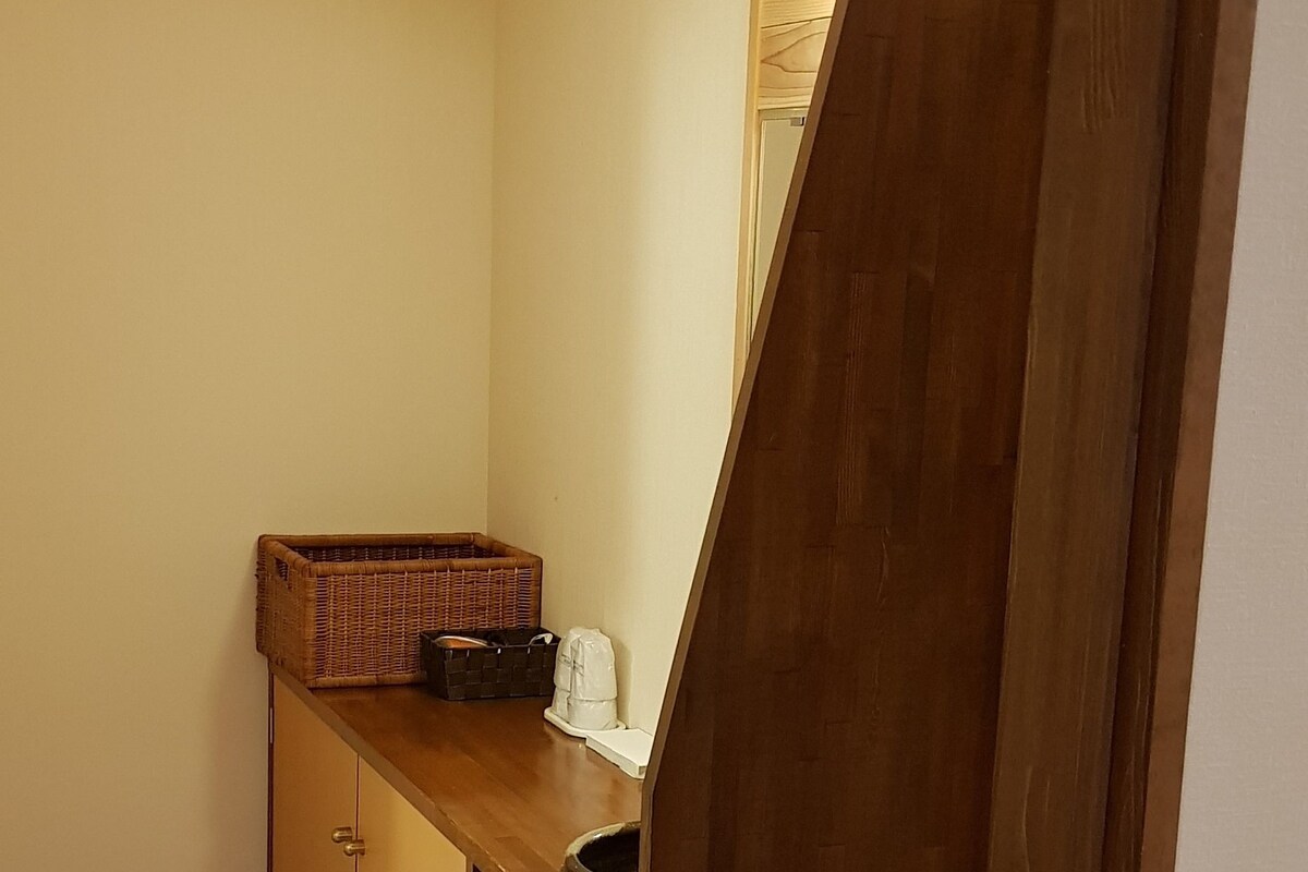 A small, narrow bathroom with wooden cabinetry, a single light fixture, and a visible trash bin.