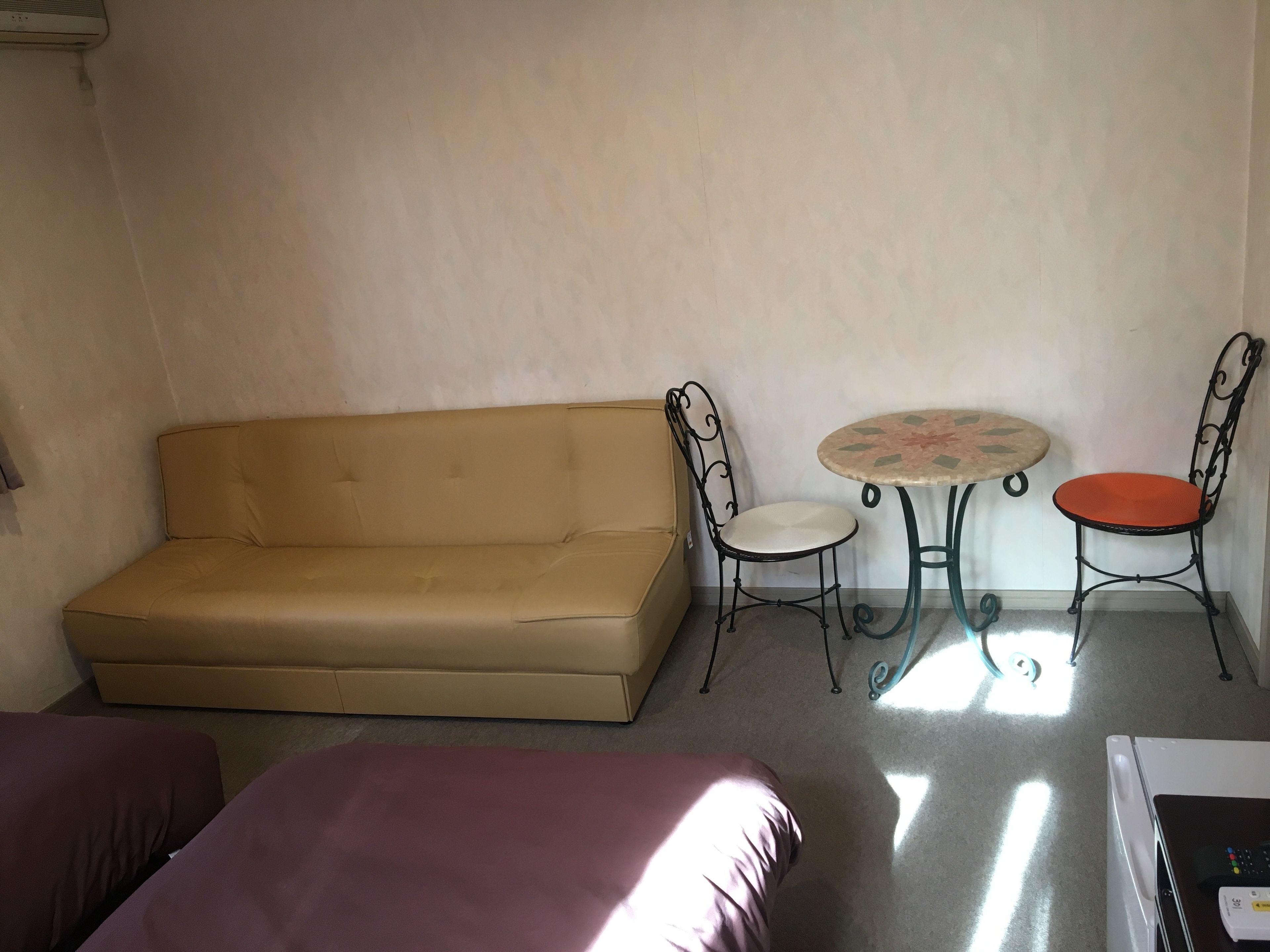 Una habitación con un sofá color beige, dos sillas, una mesita redonda y una lavadora.