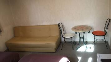 Una habitación con un sofá color beige, dos sillas, una mesita redonda y una lavadora.