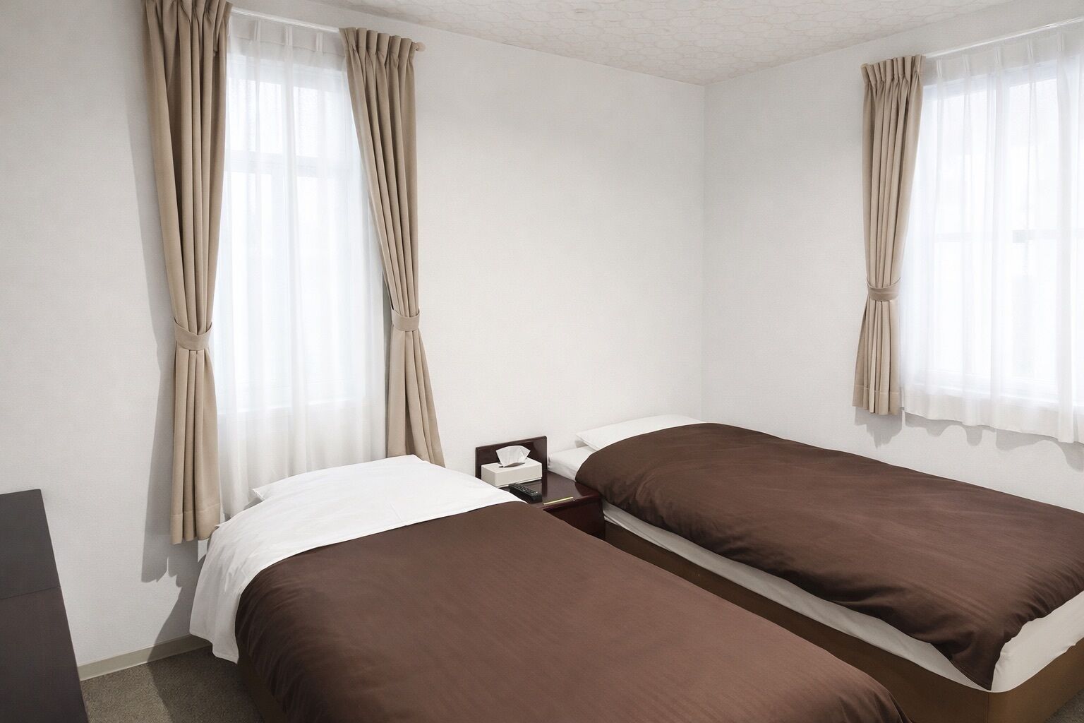 Una habitació d'hotel amb dos llits individuals, una taula de nit amb un comandament a distància i cortines a les finestres.