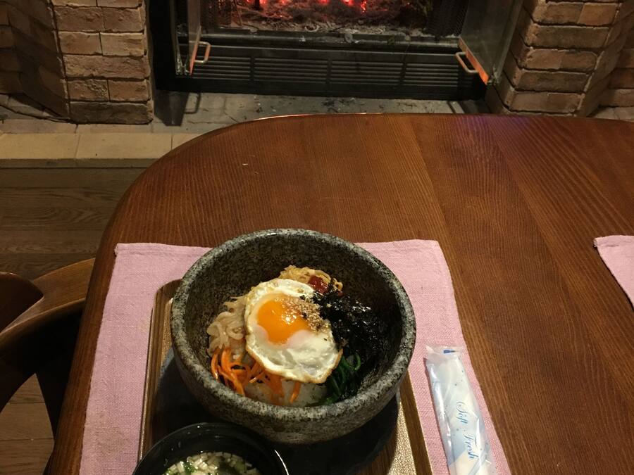A table with a meal, a spoon, and a napkin, set against a brick wall with a fireplace.
