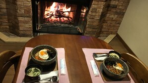 A dining table with two stone bowls of food, a fire in the background, and a brick wall. - Nikko Ikoi Hotel (Nikko)