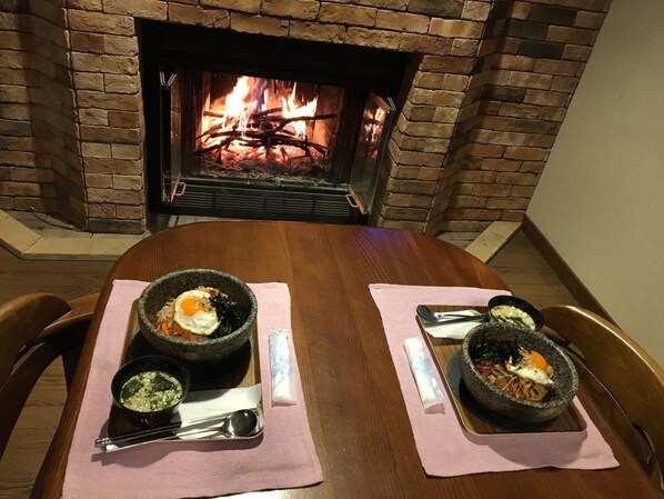 Un tavolo da pranzo con due ciotole di pietanze, un fuoco sullo sfondo e un muro in mattoni.