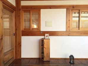 Um quarto japonês tradicional com portas de correr de madeira, uma pequena prateleira de madeira com uma fotografia e um candeeiro no chão.