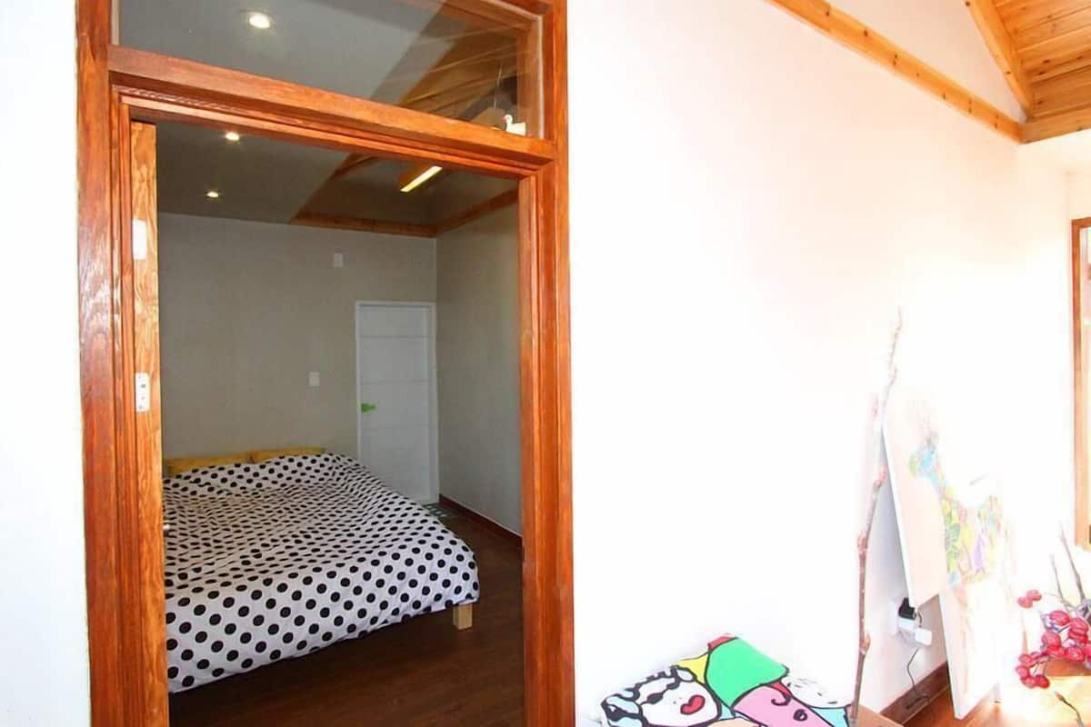 A bedroom with a bed covered in a polka dot blanket, wooden beams on the ceiling, and a white door in the background.