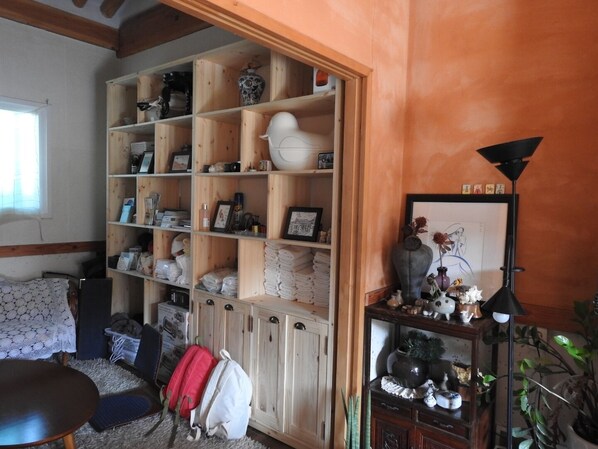 A room with a wooden cabinet filled with various items, a small table with a lamp, and a couch. - Doran Doran Guesthouse (Gyeongju)