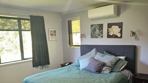 Une chambre dotée d’un grand lit, d’une fenêtre avec des rideaux, d’un climatiseur et d’œuvres d’art accrochées au mur.