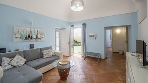 A spacious living area with a grey sofa, a glass coffee table, and a painting on the wall.